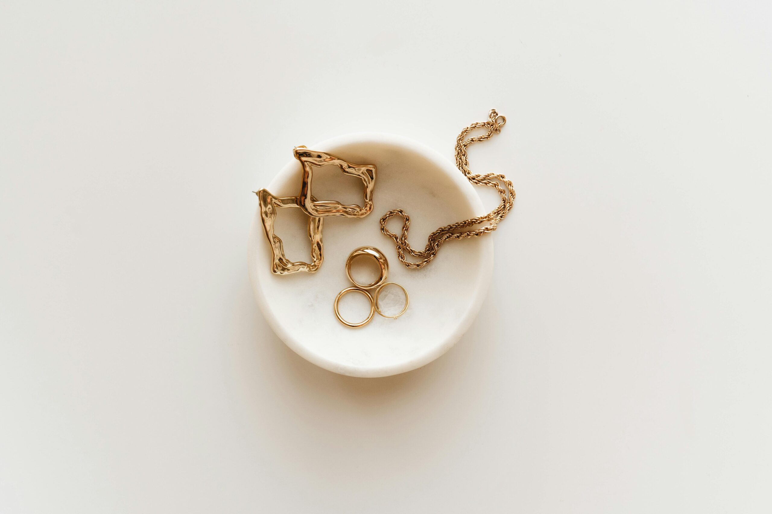 Stylish arrangement of gold jewelry including rings, earrings, and a necklace on a marble dish.